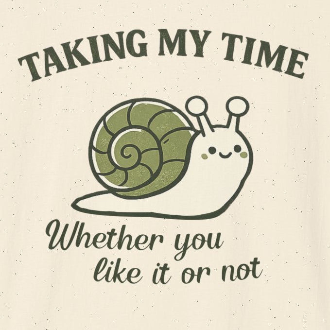 An off-white short-sleeve crewneck t-shirt featuring a graphic of a cartoon snail with a green shell and the text 'TAKING MY TIME' and 'Whether you like it or not' in dark green and black fonts.