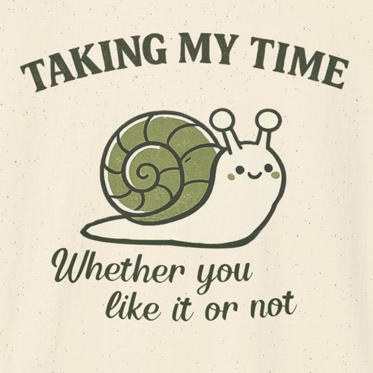 An off-white short-sleeve crewneck t-shirt featuring a graphic of a cartoon snail with a green shell and the text 'TAKING MY TIME' and 'Whether you like it or not' in dark green and black fonts.