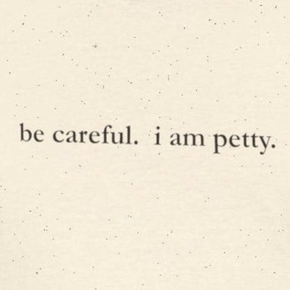 Person wearing cream t-shirt with 'be careful. i am petty" small, black text.
