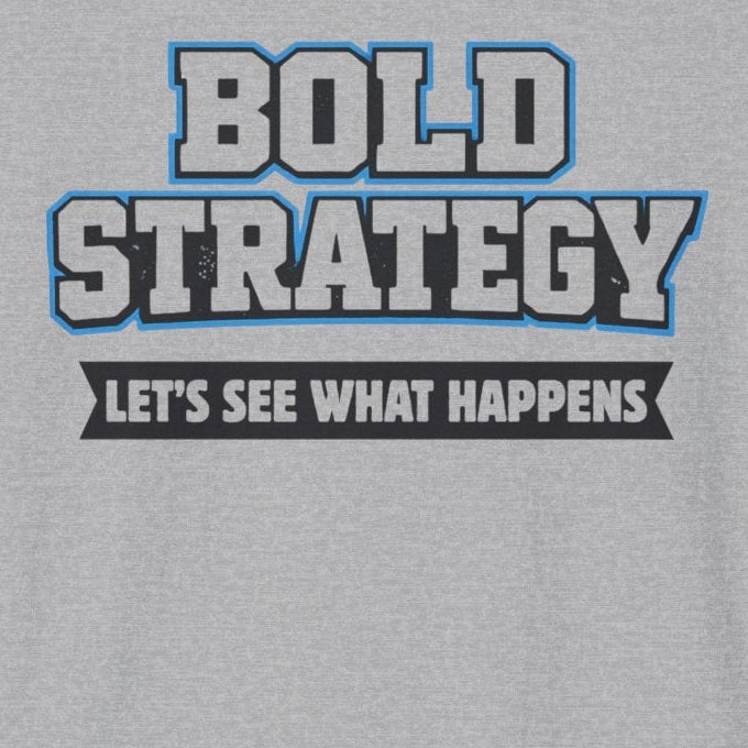 A light gray heather crewneck t-shirt featuring a graphic print on the chest that reads 'BOLD STRATEGY' in blue and white block letters, with the phrase 'LET'S SEE WHAT HAPPENS' below it in white text on a black bar.
