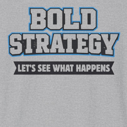 A light gray heather crewneck t-shirt featuring a graphic print on the chest that reads 'BOLD STRATEGY' in blue and white block letters, with the phrase 'LET'S SEE WHAT HAPPENS' below it in white text on a black bar.